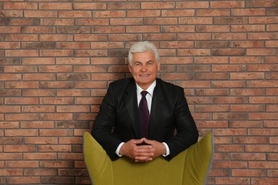Photo of Happy mature businessman standing near armchair against brick wall