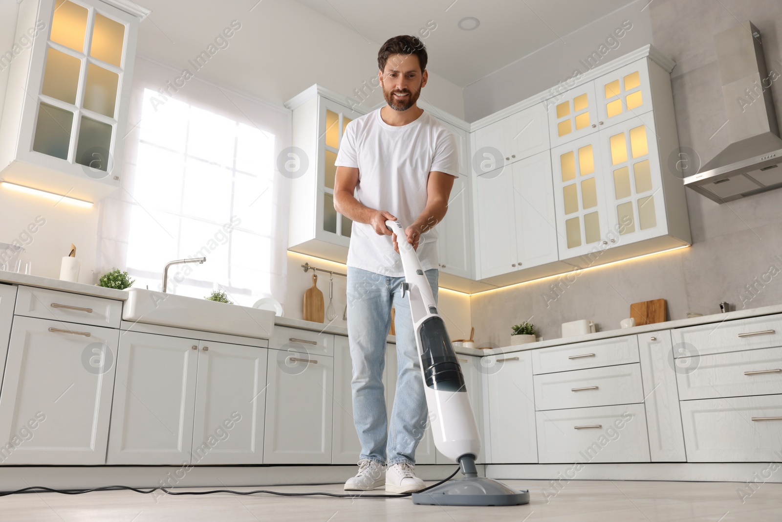 Photo of Happy man cleaning floor with steam mop in kitchen at home, low angle view