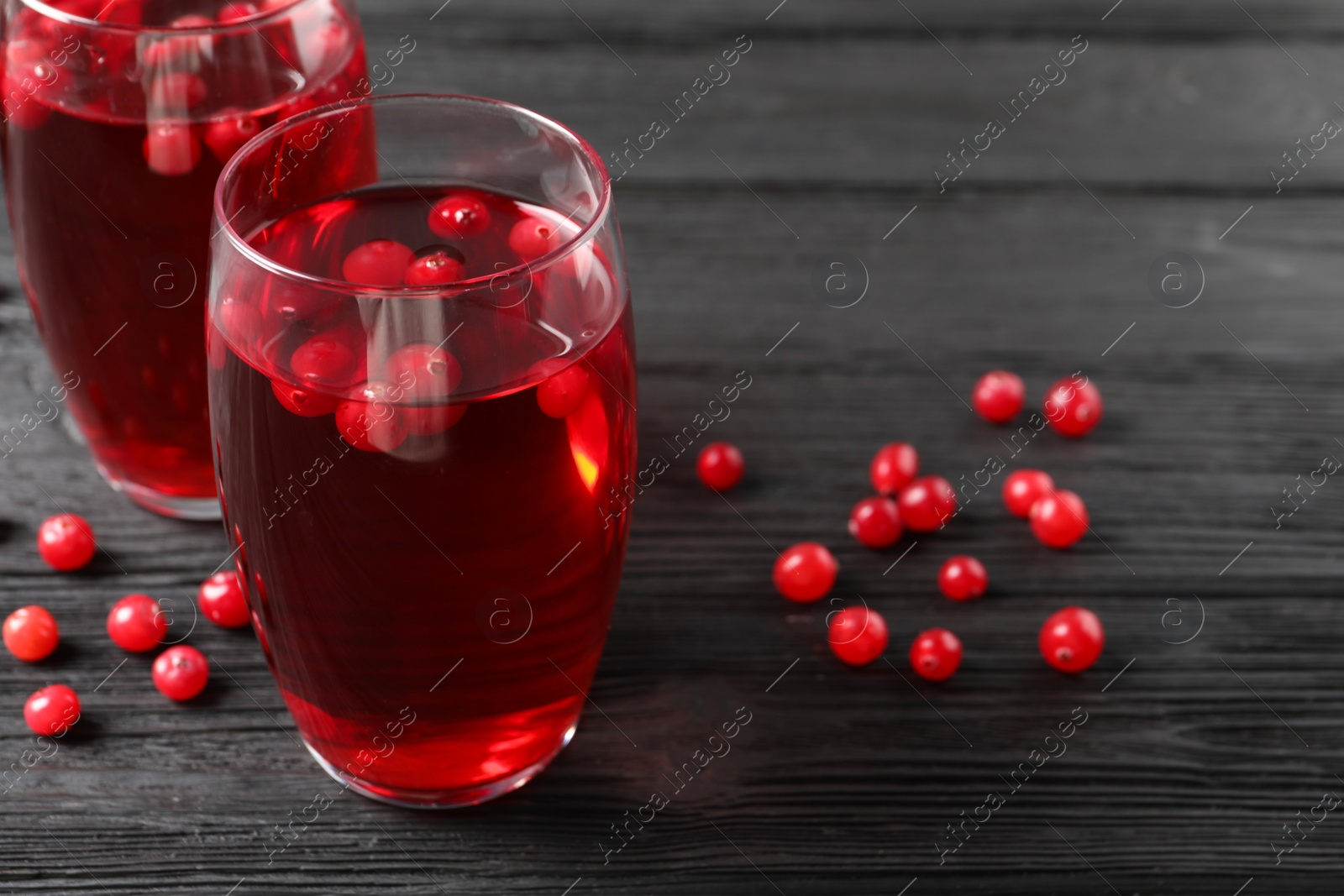 Photo of Tasty cranberry juice in glasses and fresh berries on black wooden table, closeup. Space for text