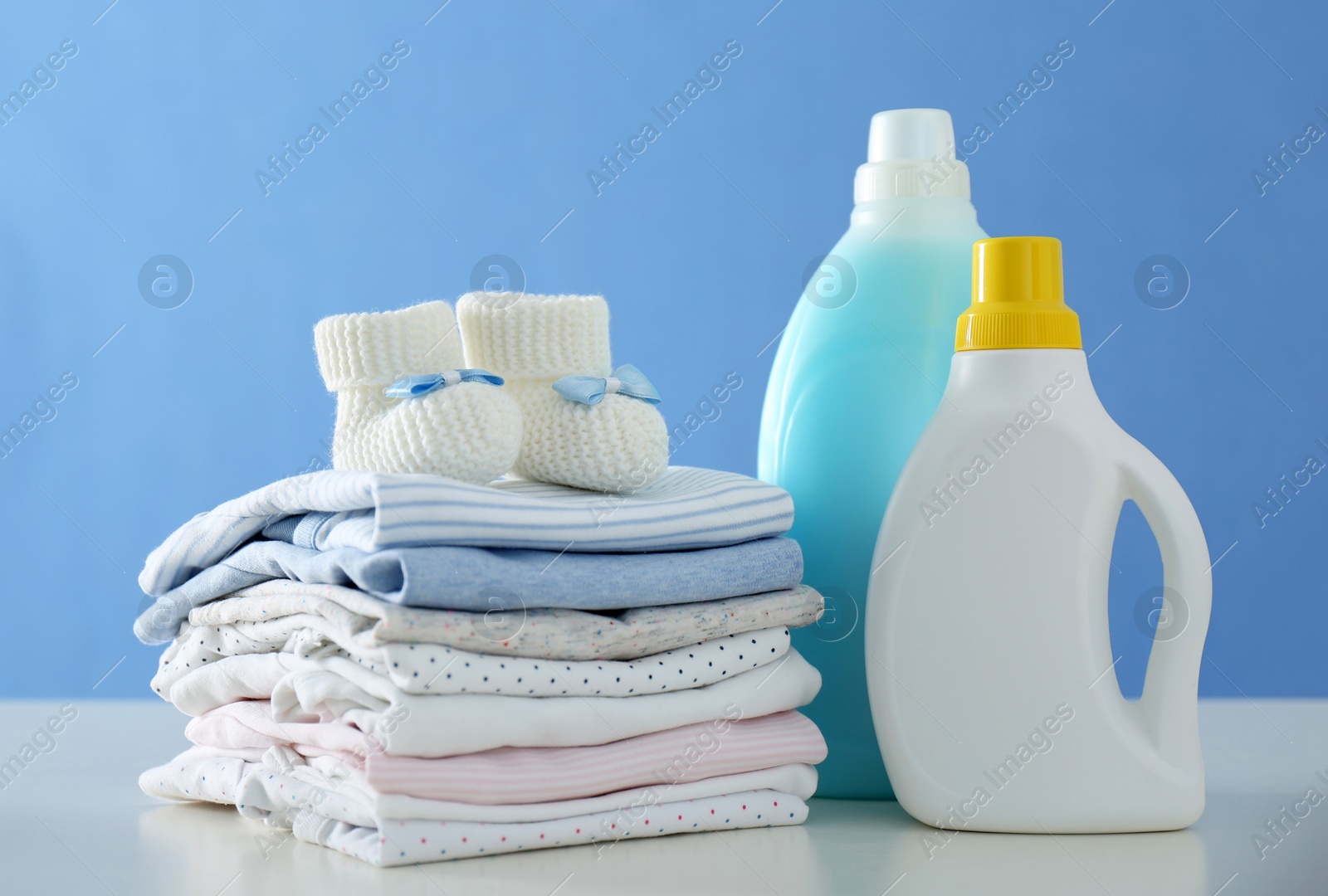 Photo of Detergents and children's clothes on white table near blue wall