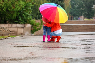 Photo of Mother and daughter with bright umbrella under rain outdoors