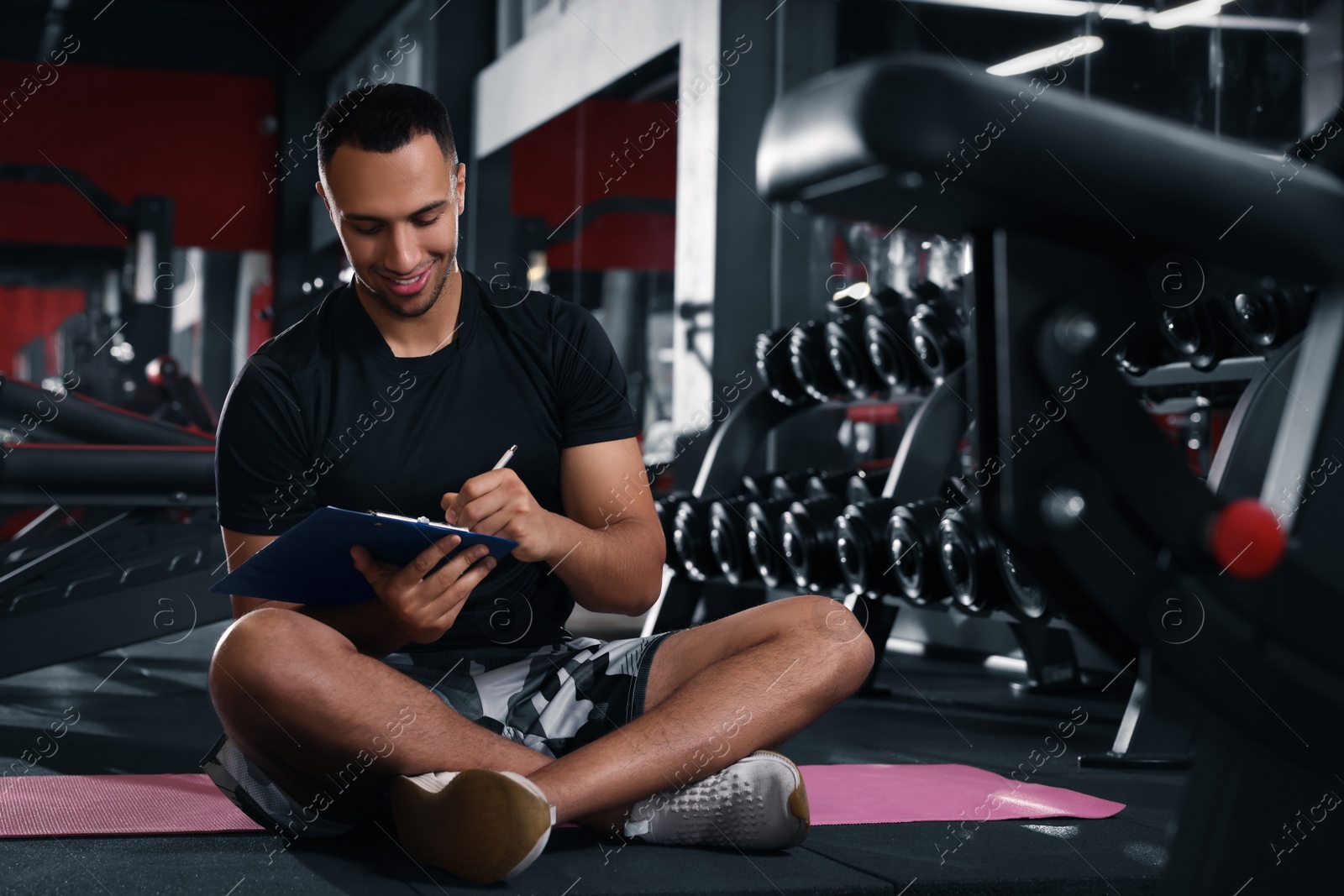 Photo of Happy trainer writing down workout plan in modern gym, space for text