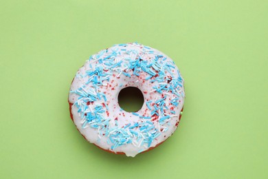 Photo of Glazed donut decorated with sprinkles on green background, top view. Tasty confectionery