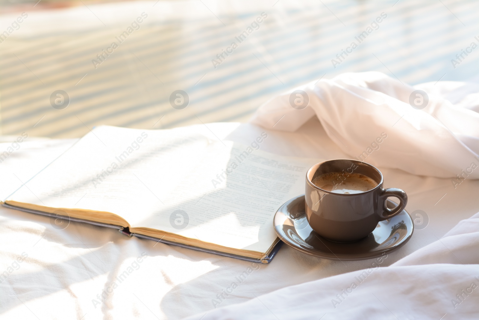 Photo of Aromatic morning coffee and open book on bed indoors