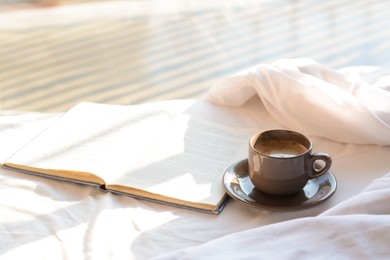 Aromatic morning coffee and open book on bed indoors