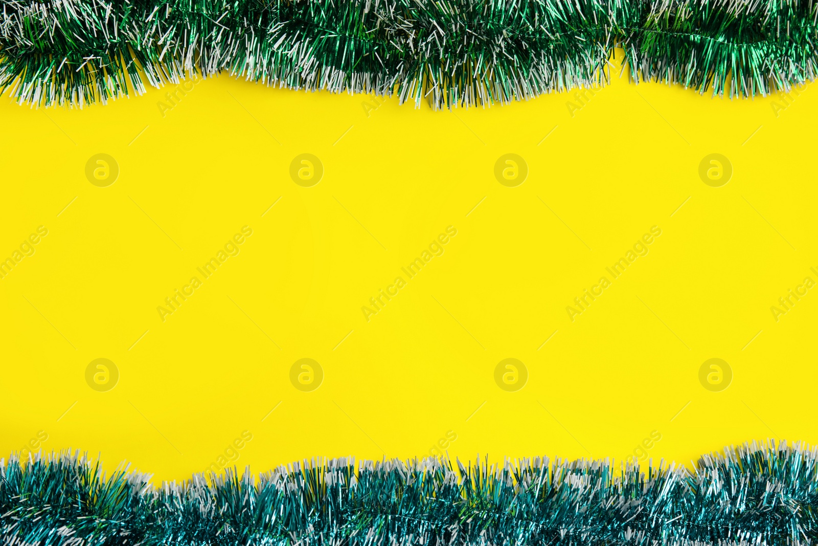 Photo of Shiny bright tinsel on yellow background, flat lay. Space for text