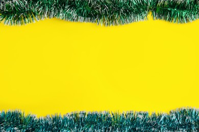 Shiny bright tinsel on yellow background, flat lay. Space for text