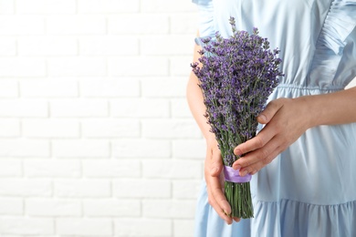 Photo of Woman holding fresh lavender flowers against white brick wall, closeup. Space for text