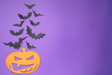 Photo of Flat lay composition with paper bats and pumpkin on purple background, space for text. Halloween decor