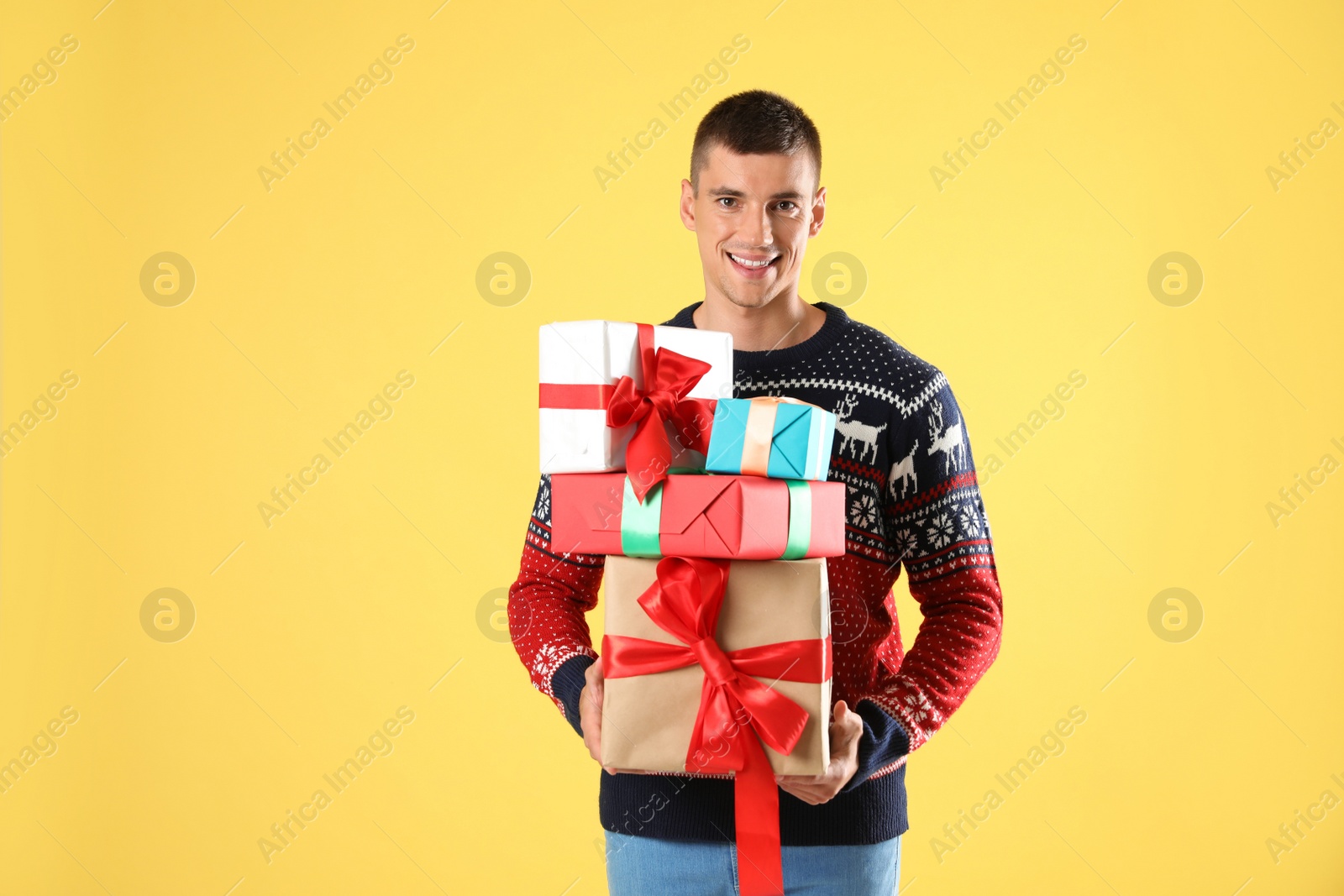 Photo of Happy man in Christmas sweater holding gift boxes on yellow background