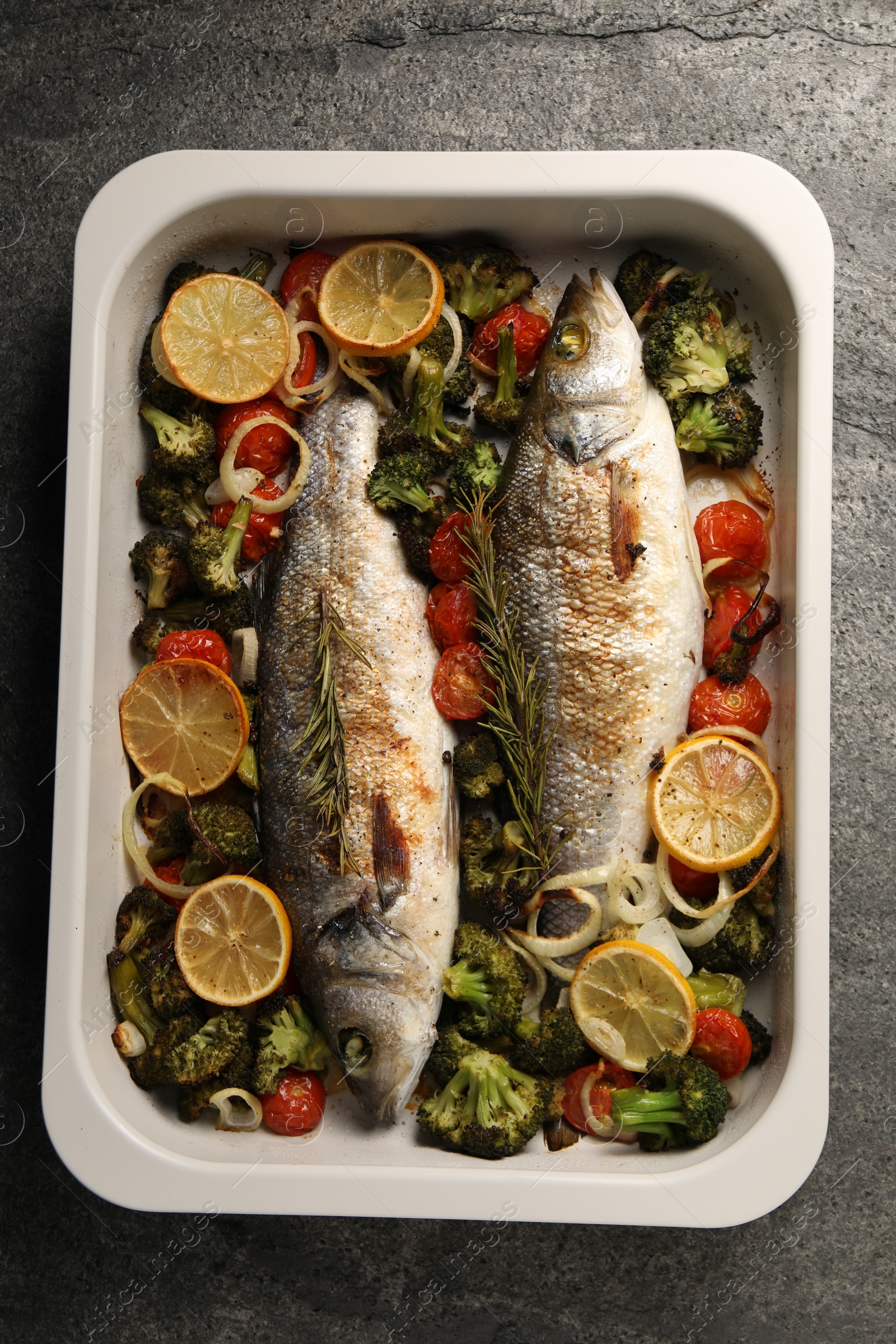 Photo of Delicious fish with vegetables and lemon in baking dish on grey textured table, top view