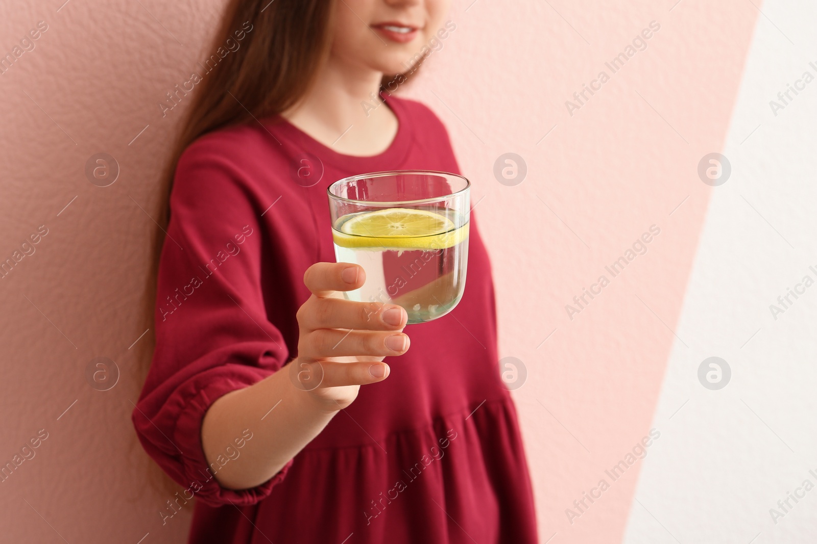 Photo of Young woman holding glass of lemon water on color background