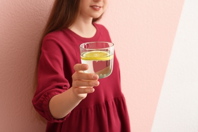 Young woman holding glass of lemon water on color background