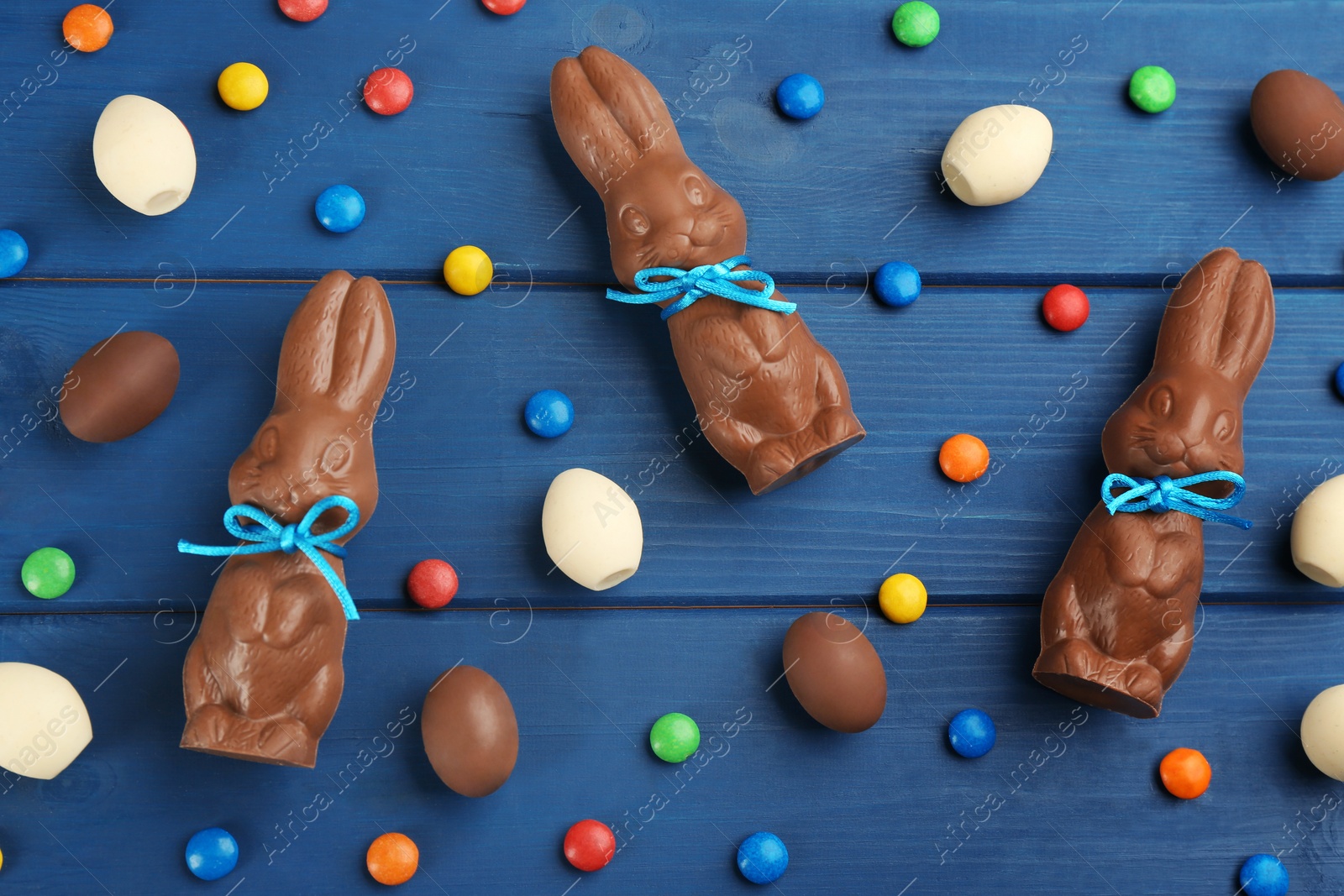 Photo of Chocolate Easter bunnies, candies and eggs on blue wooden table, flat lay