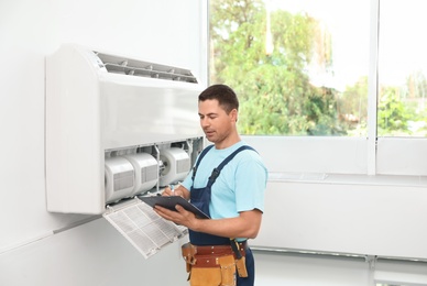 Photo of Technician with clipboard near air conditioner indoors