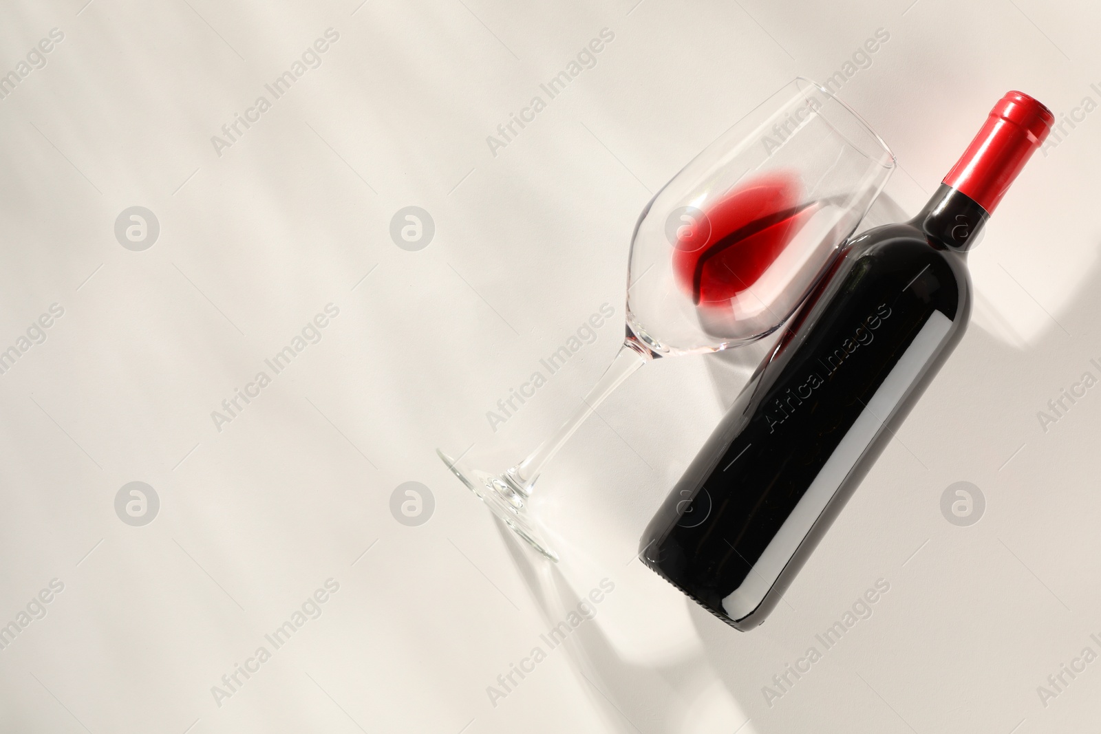 Photo of Bottle of expensive red wine and wineglass on light background, top view. Space for text