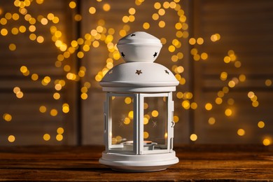 Beautiful white decorative lantern on wooden table against blurred lights