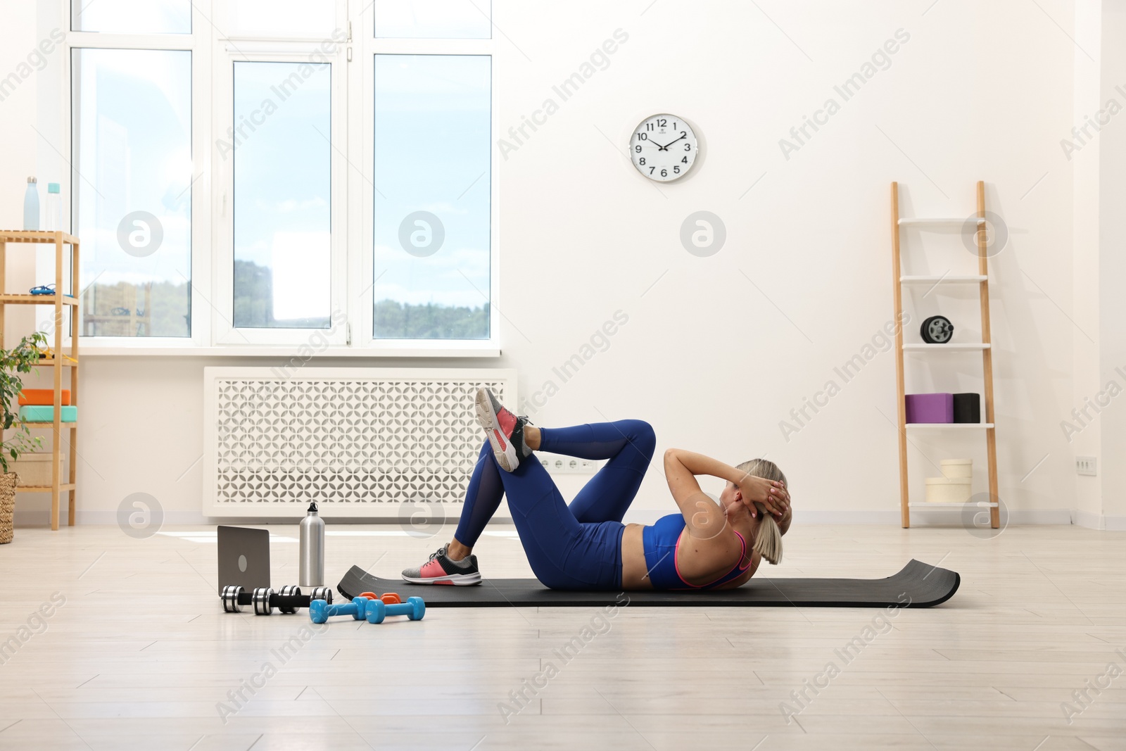 Photo of Online fitness trainer. Woman pumping up abs near laptop at home