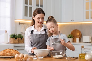 Making bread. Mother and her daughter preparing dough at wooden table in kitchen