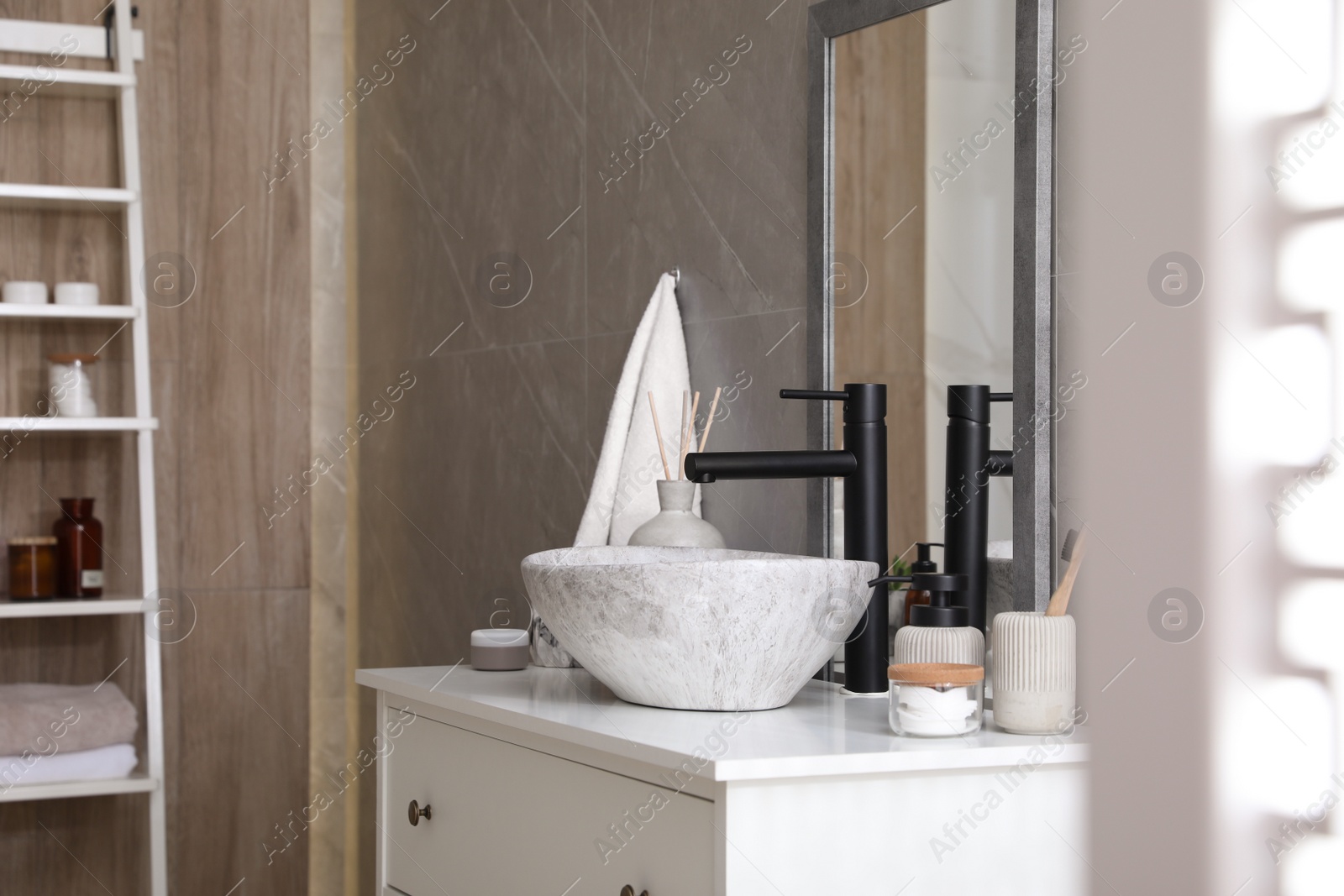 Photo of Stone vessel sink with faucet and toiletries on white countertop in bathroom