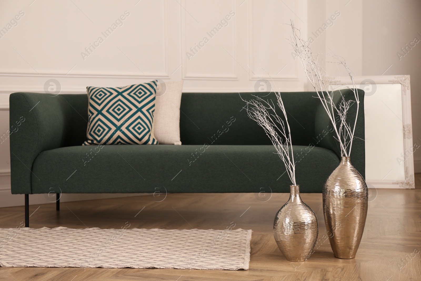 Photo of Metal vases with white tree twigs on floor near sofa in living room