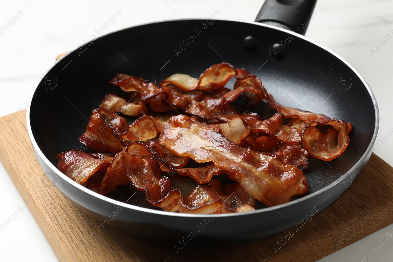 Photo of Delicious bacon slices in frying pan on white table, closeup