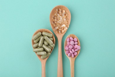 Different vitamin pills in wooden spoons on turquoise background, flat lay