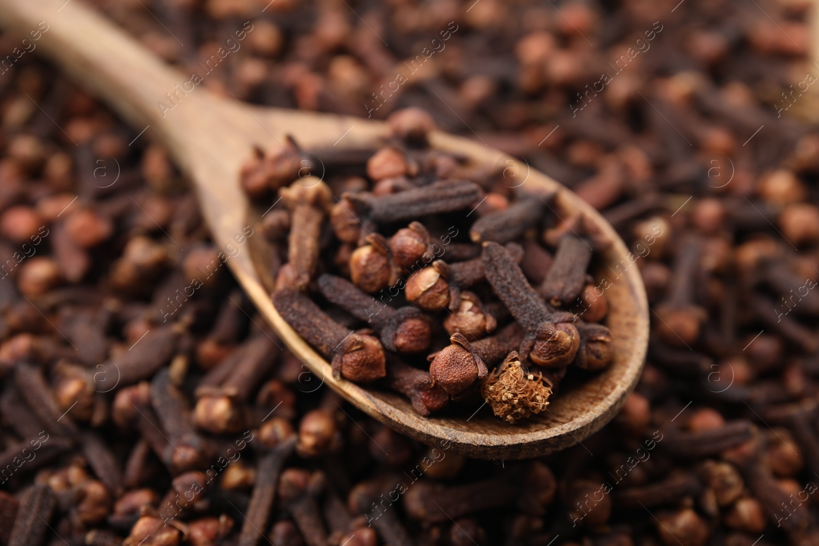 Photo of Many aromatic cloves and wooden spoon as background, closeup