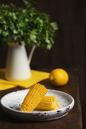 Photo of Plate with ripe corn cobs on table against dark background. Space for text