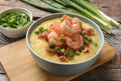 Photo of Fresh tasty shrimps, bacon, grits and green onion in bowl on wooden table, closeup