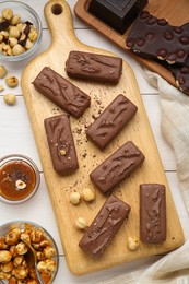 Photo of Delicious chocolate candy bars, caramel and nuts on white wooden table, flat lay