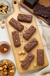 Delicious chocolate candy bars, caramel and nuts on white wooden table, flat lay