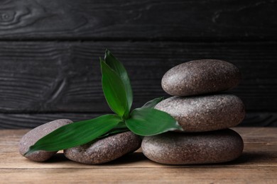 Photo of Spa stones with bamboo leaves on wooden table. Space for text