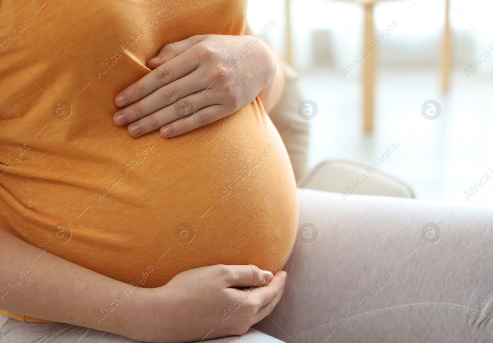 Photo of Pregnant woman sitting in light room at home, closeup