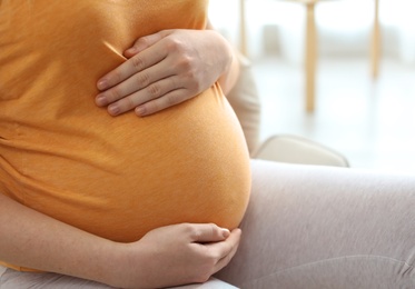 Photo of Pregnant woman sitting in light room at home, closeup