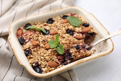 Photo of Tasty baked oatmeal with berries and almonds in baking tray on white tiled table, closeup