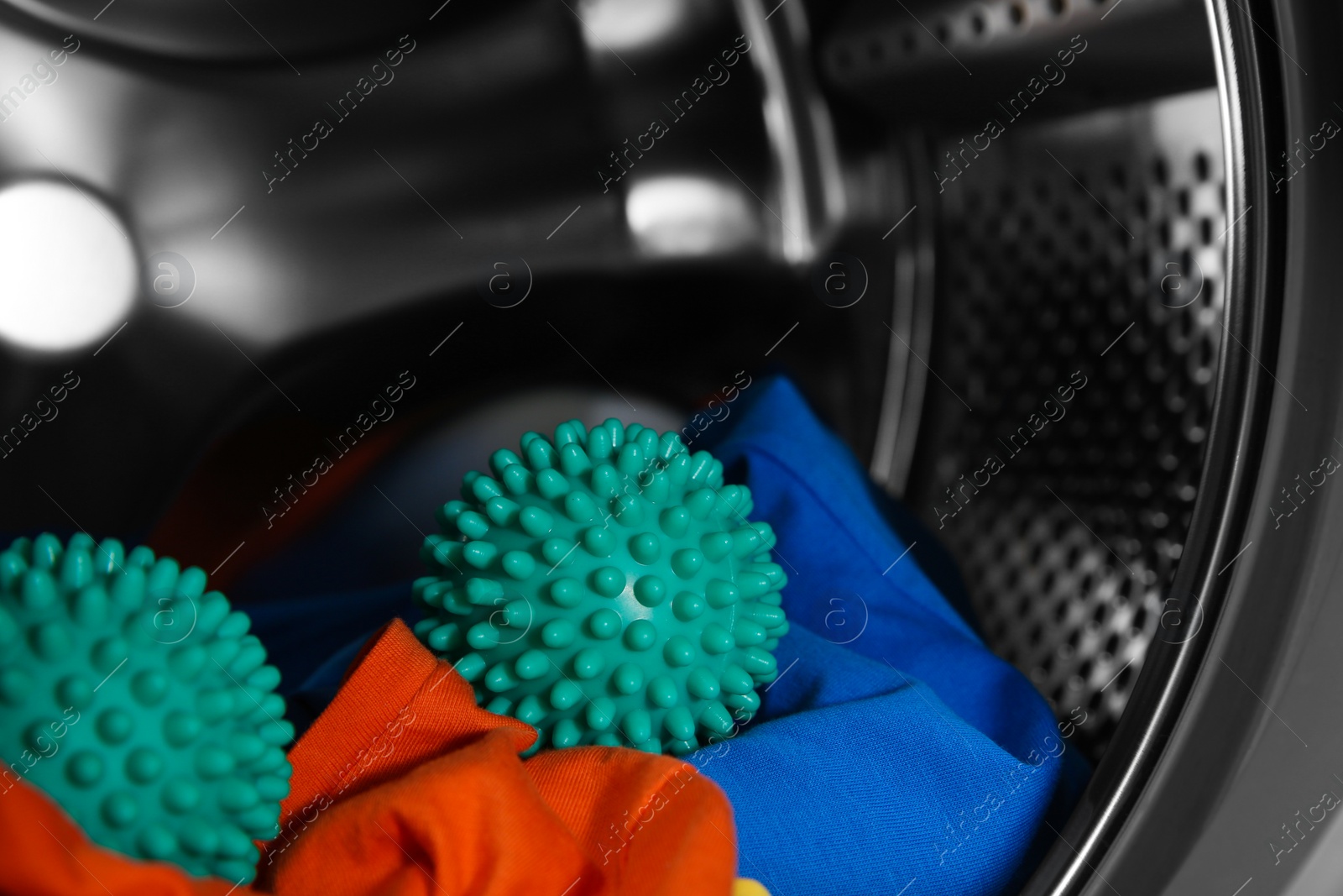 Photo of Green dryer balls and clothes in washing machine drum, closeup