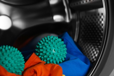 Photo of Green dryer balls and clothes in washing machine drum, closeup