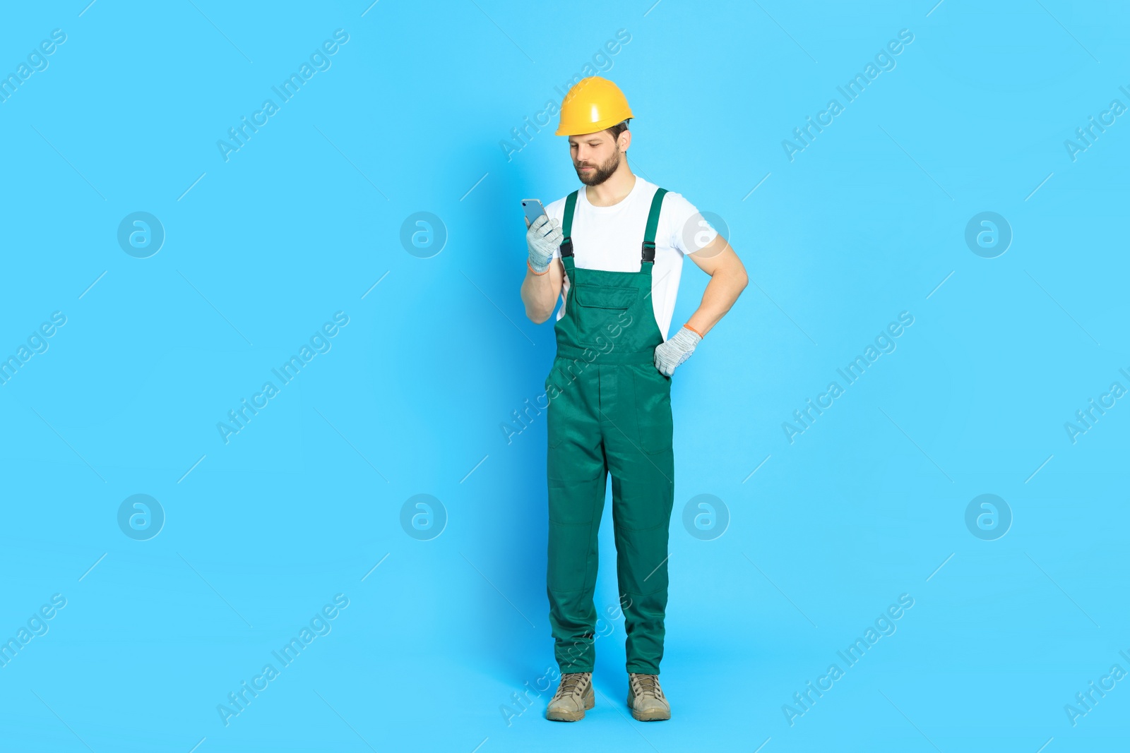 Photo of Professional repairman in uniform with smartphone on light blue background