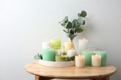 Composition with burning candles on table near white wall