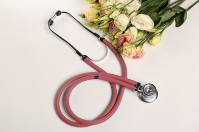 Stethoscope and eustoma flowers on white background, flat lay. Happy Doctor's Day