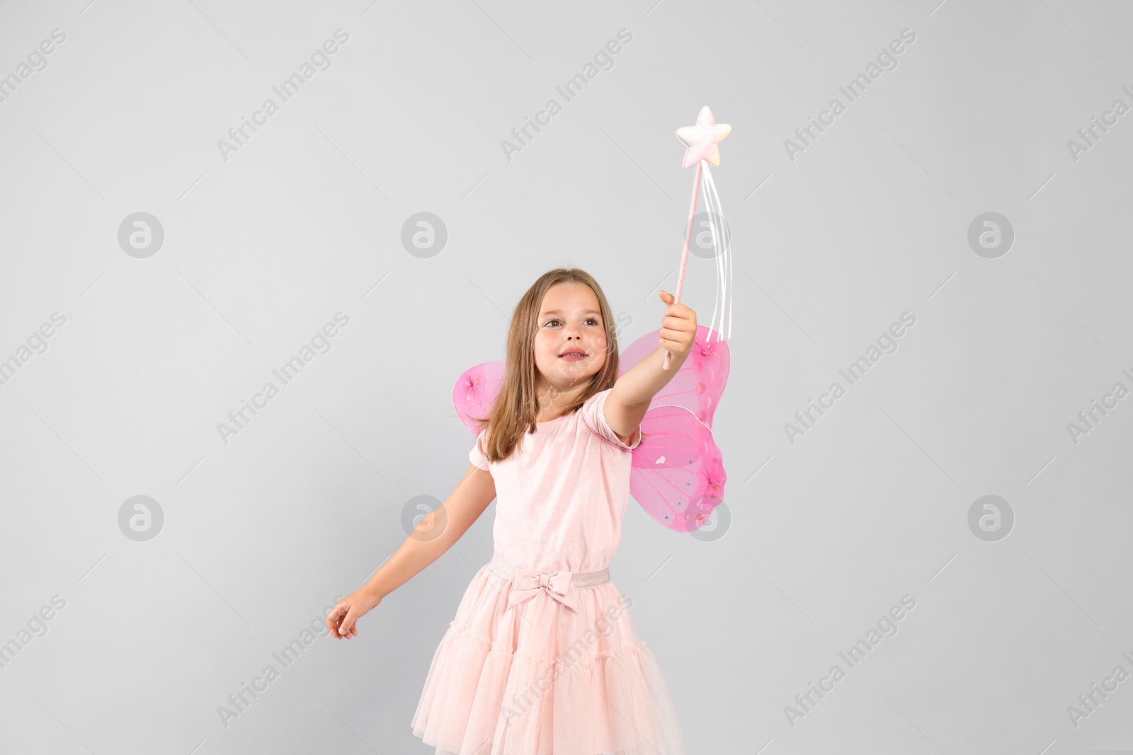 Photo of Cute little girl in fairy costume with pink wings and magic wand on light background