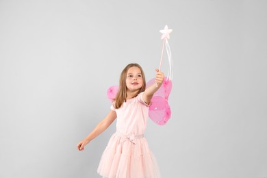 Cute little girl in fairy costume with pink wings and magic wand on light background