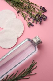 Flat lay composition with bottle of makeup remover and cotton pads on pink background