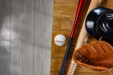 Baseball bats, batting helmet, leather glove and ball on wooden bench indoors, top view. Space for text