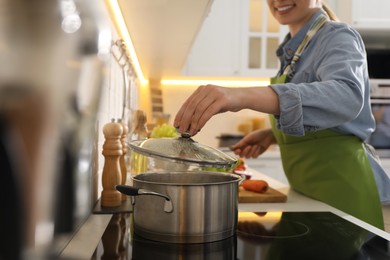 Woman opening pot with fresh bouillon in kitchen, closeup. Homemade recipe