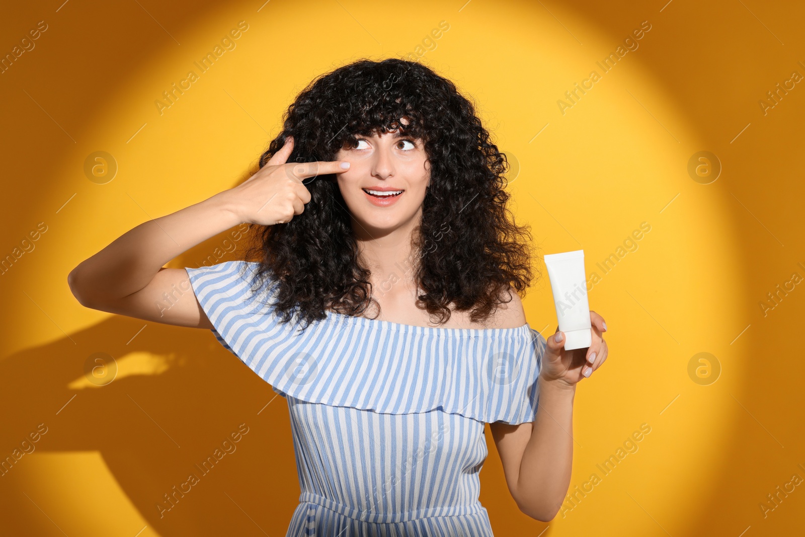 Photo of Beautiful young woman with tube of sunscreen in sunlight on orange background