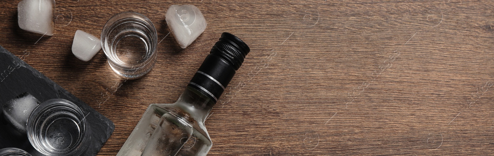 Image of Bottle of vodka, shot glasses and ice cubes on wooden table, flat lay with space for text. Banner design