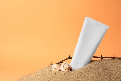 Photo of Tube with cream, shells and branches on sand against orange background, space for text. Cosmetic product