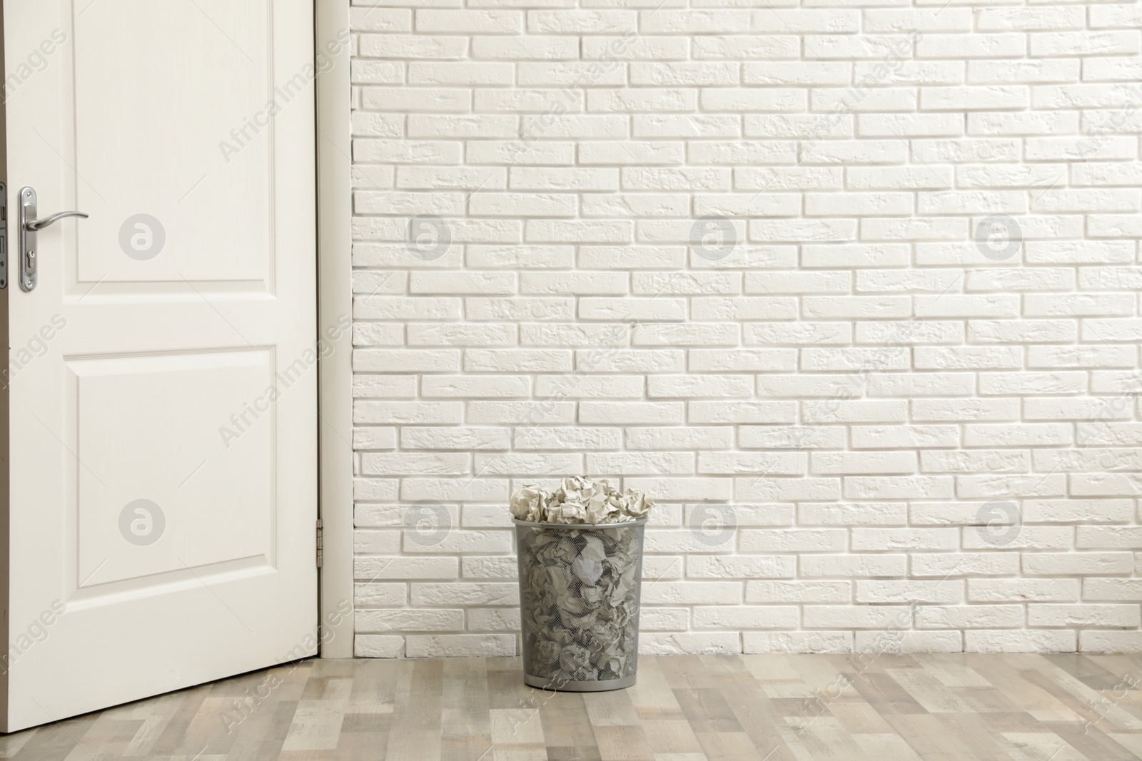 Photo of Metal bin with crumpled paper on floor against brick wall, space for text